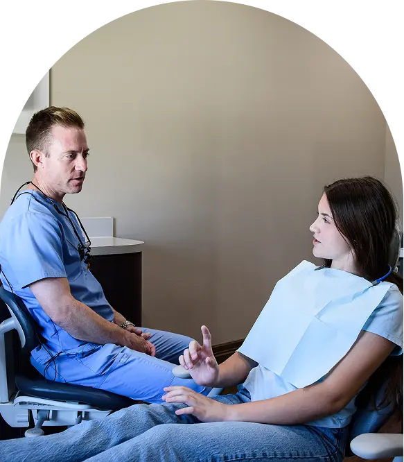 Dentist in light blue scrubs attentively listening to a patient during a consultation in a modern dental office, highlighting compassionate care and open communication